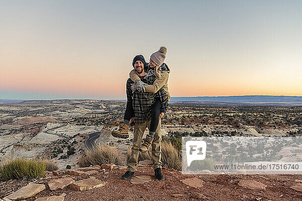 Happy man piggybacking woman in desert during sunset