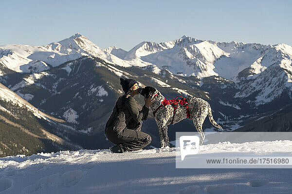 female hiker kissing dog on snow covered mountain during vacation
