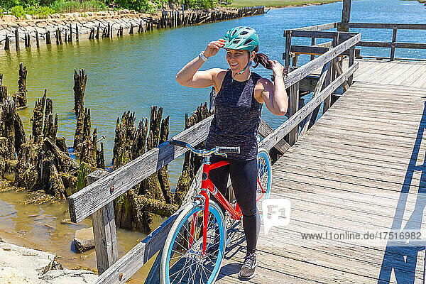 Woman with Ponytail Adjusts Bike Helmet on Dock Near Water