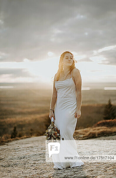 smiling bride in evening sun on mountain summit with flowers