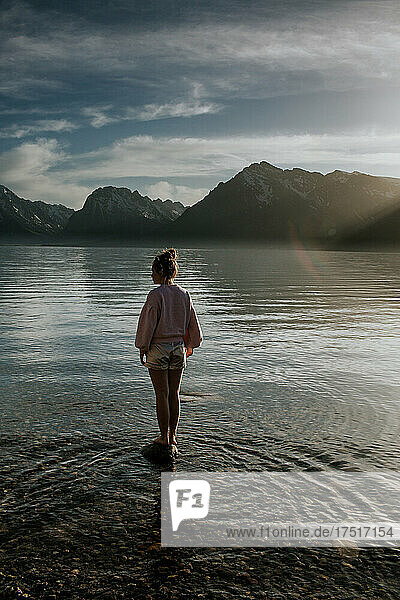 Teen girl standing on rock in lake at base of mountains