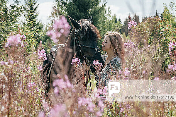 Young woman in meadow in flowers stroking horse.