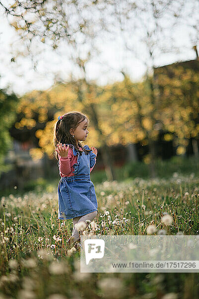 Young girl playing in a park full of dandelions with a blurry ba