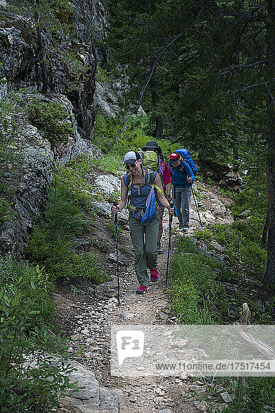 A female backpacker laughs while hiking up a trail with two others