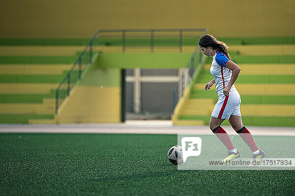 young female soccer player kicks the ball on the field
