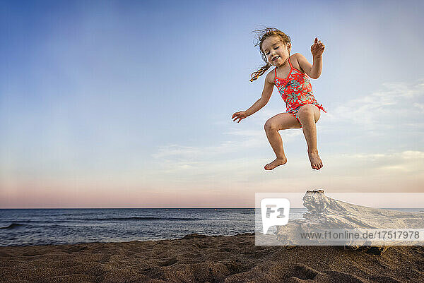 Small girl jumping off driftwood at beach in summer