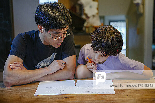 A boy and father sit together at kitchen table doing homework