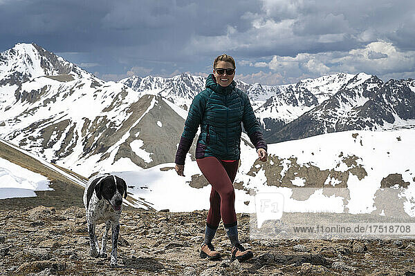 Happy female hiker hiking with dog on mountain against cloudy sky