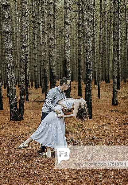 man dances and dips woman in white dress in pine tree forest  Michigan