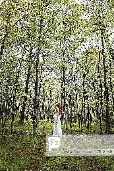 Woman in white dress standing alone in a clearing in the woods.