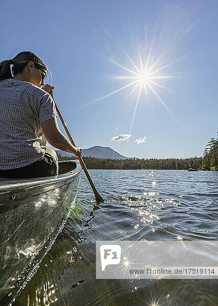 Young woman paddles canoe on Daicey Pond  Maine. Katahdin in distance.