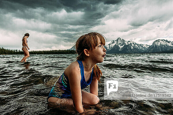 Amazed young girl looking at mountains while sitting in lake