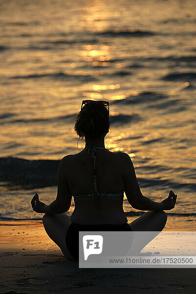 Woman practising yoga meditation on beach at sunset as concept for silence and relaxation  United Arab Emirates  Middle East