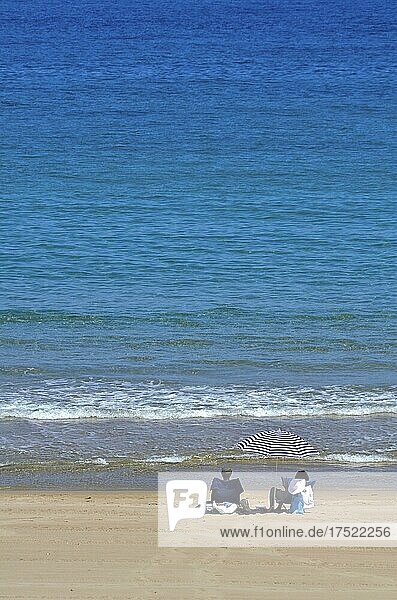 Mann und Frau unter Sonnenschirm am Strand an Wassersaum vom Meer  Quatro Calas  Hospitalet dEnfant  Katalonien  Spanien  Europa