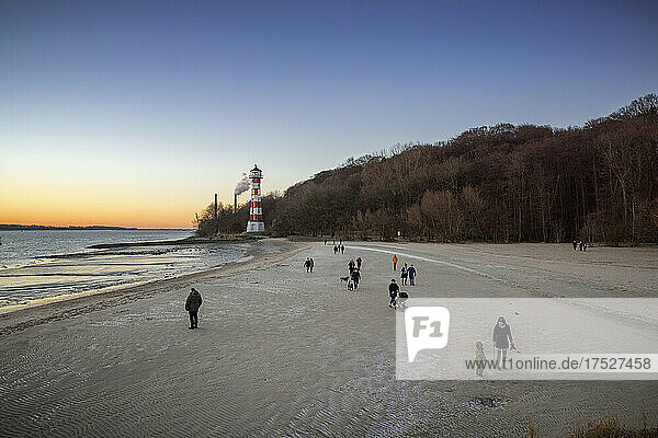 Icy winter afternoon on the beach of Wittenbergen in Hamburg-Rissen. The setting sun illuminates the lighthouse. In the background the chimneys of the coal-fired power plant Wedel