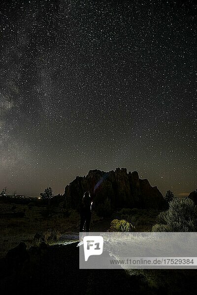 Junge Frau auf einem Weg leuchtet mit Taschenlampe  Canyon vor Nachthimmel  Sternenhimmel mit Milchstraße  Smith Rock State Park  Oregon  USA  Nordamerika