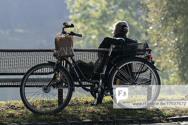 Eine Dame genießt auf einer Parkbank die wärmende Herbstsonne im Olympiapark München  Bayern  Deutschland  Europa