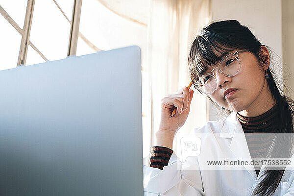 Young chemist thinking while looking at laptop in laboratory