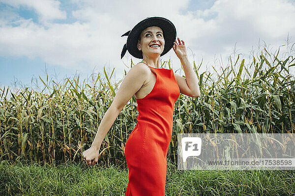 Smiling beautiful woman with hat standing in front of corn field