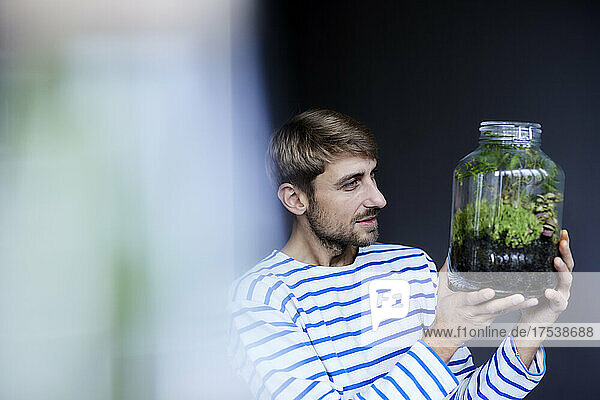 Man looking at plant in glass jar