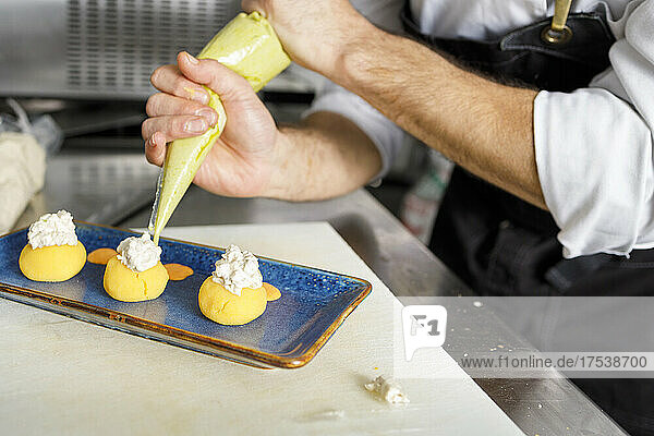 Chef decorating dessert with whipped cream on tray at kitchen counter