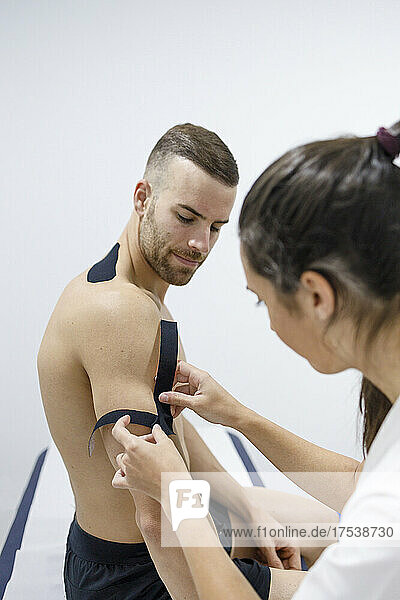 Physical therapist applying therapeutic tape on sportsman's muscle