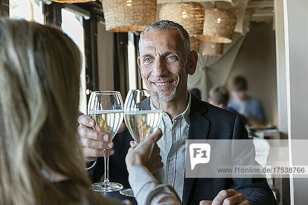 Lächelnder Mann prostet beim Mittagessen im Restaurant mit einer Frau ein Glas Champagner an