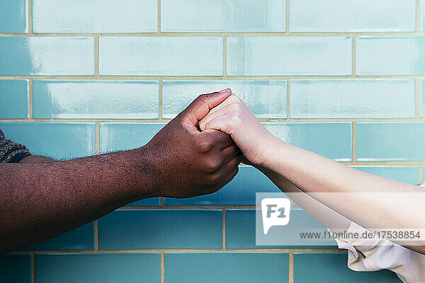 Man holding woman's hands in front of turquoise brick wall