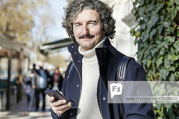 Smiling man holding smart phone on sunny day
