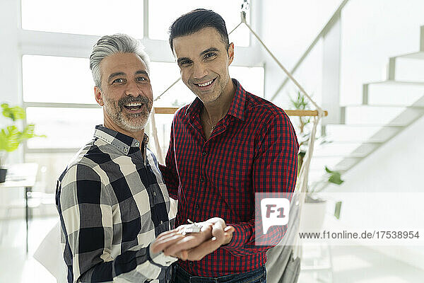 Happy gay couple holding new house key at home