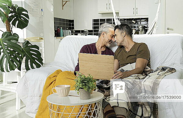Loving gay couple with laptop romancing at home