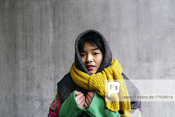 Young woman wearing scarf in front of wall