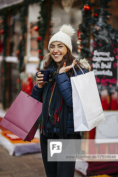 Woman holding shopping bags and mug laughing in front of store