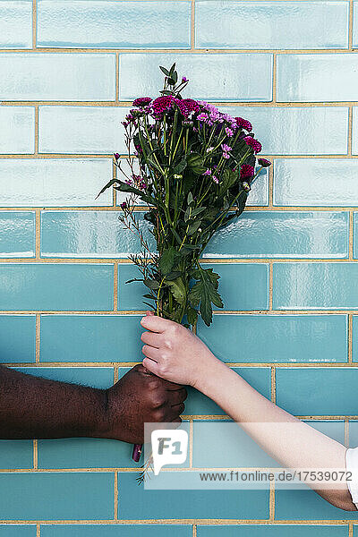 Man and woman holding bouquet on turquoise brick wall