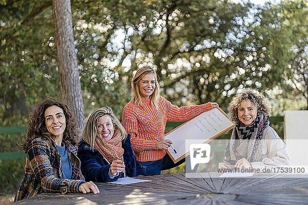Smiling woman holding whiteboard by friends at park