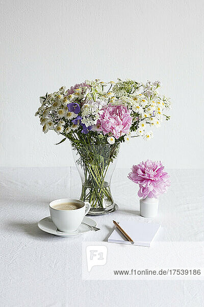 Studio shot of cup of coffee and bouquet of peonies  feverfews (Tanacetum parthenium)  bellflowers (Campanula) and white laceflowers (Orlaya grandiflora)