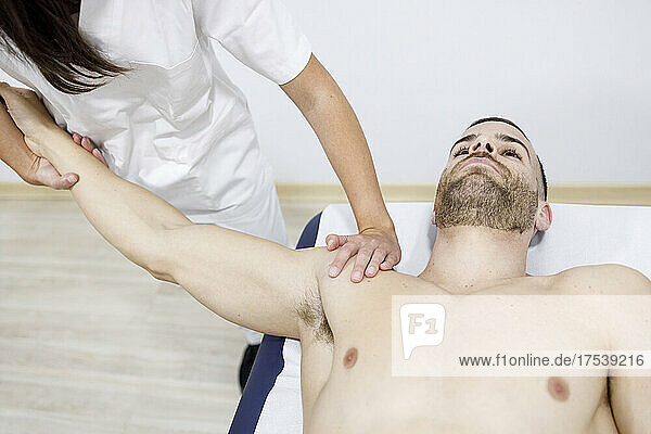 Physical therapist stretching sportsman's hand on massage table