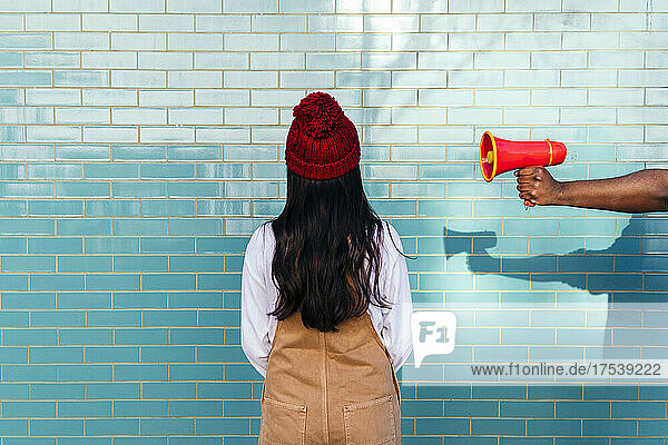 Man's hand holding megaphone by woman facing turquoise brick wall