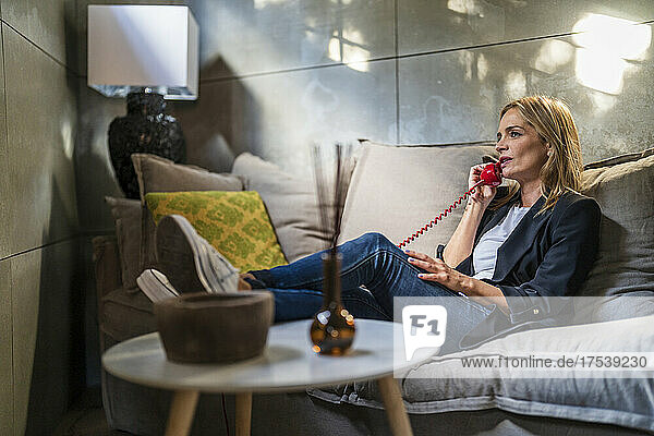 Businesswoman talking through landline phone sitting on sofa at office