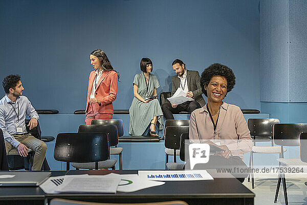 Happy businesswoman with colleagues discussing in background at office