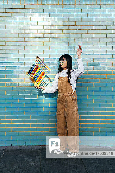 Young woman balancing abacus in front of brick wall