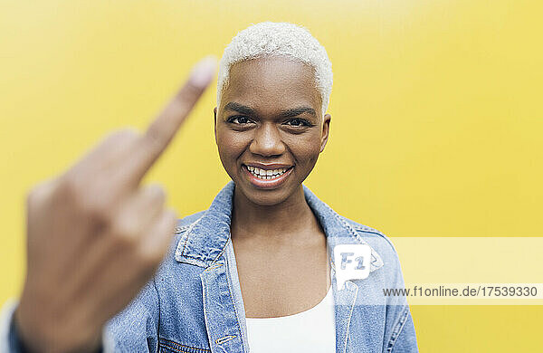 Smiling woman showing middle finger against yellow background