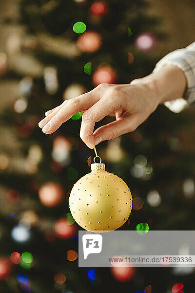 Woman holding bauble in front of christmas tree at home