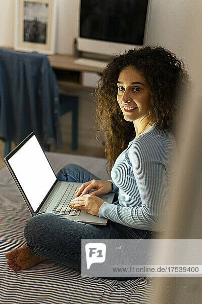 Young woman with laptop in bedroom at home