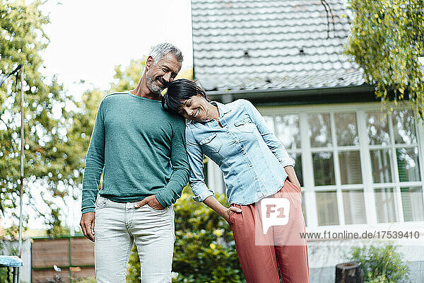 Smiling woman with hands in pockets leaning on man's shoulder