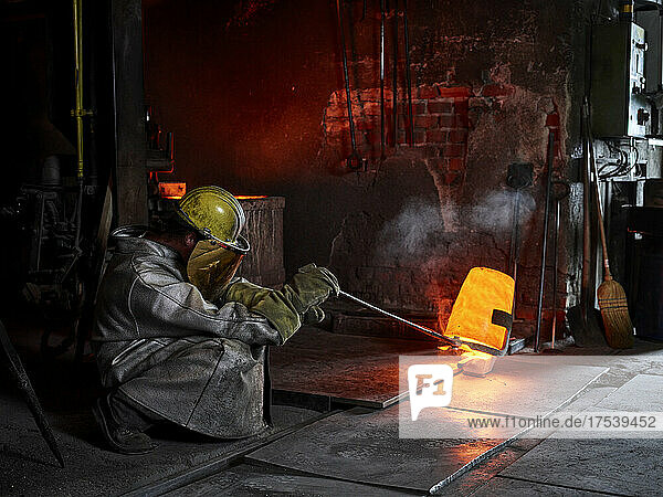 Craftsperson wearing protective workwear pouring cast metal in steel mill