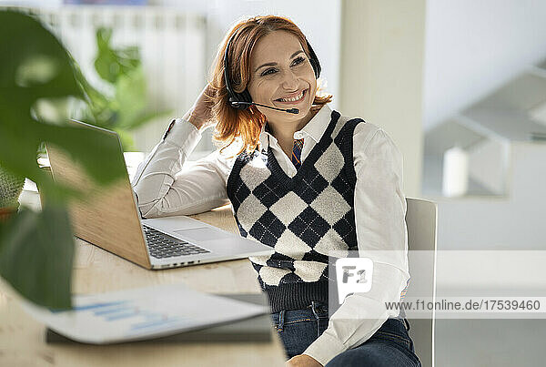 Businesswoman with headset sitting at desk with laptop in home office