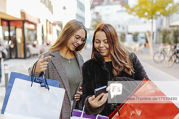 Happy women with shopping bags looking at smart phone