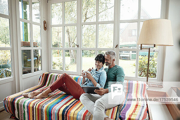Man sharing tablet PC with woman holding coffee cup on sofa