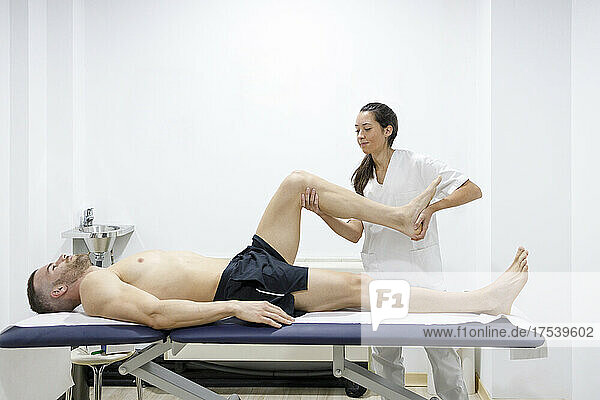 Massage therapist stretching sportsman's leg on table